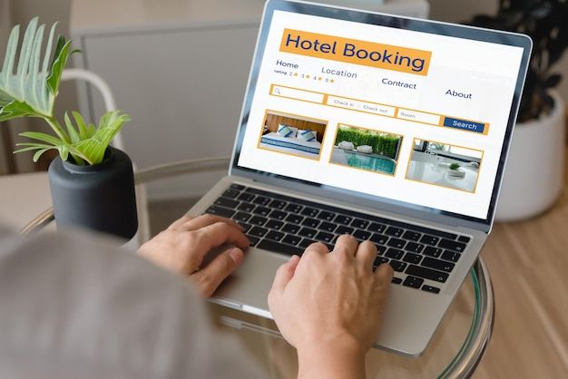 En person bokar hotell via en laptop på ett glasbord.